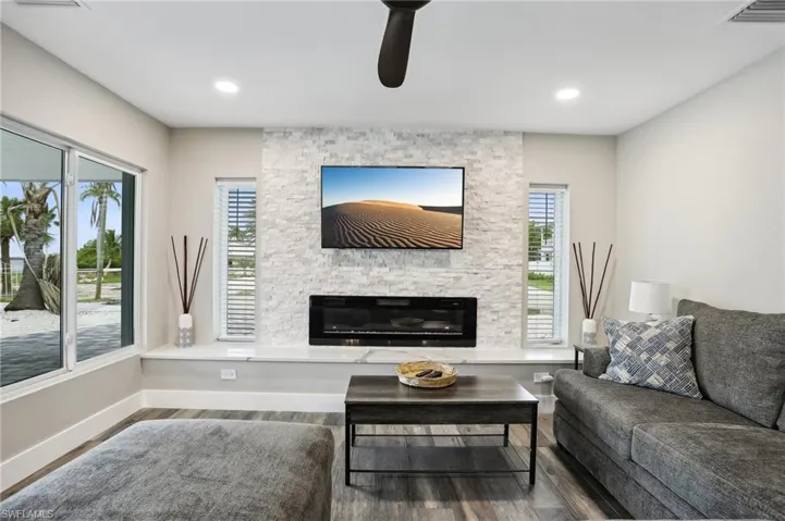 Living room with a stone fireplace, ceiling fan, and hardwood / wood-style floors