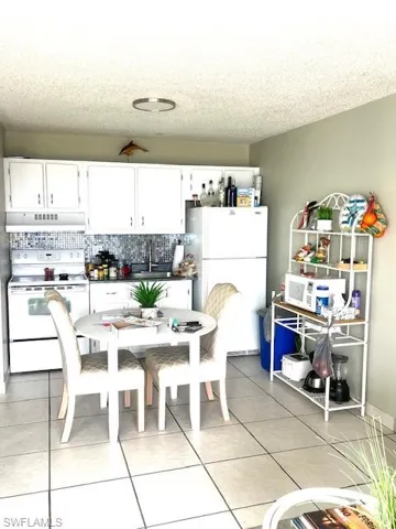 Kitchen with white appliances, white cabinetry, dark countertops, backsplash, and light tile patterned floors