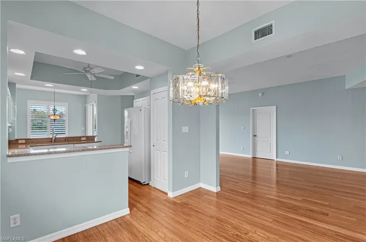 Kitchen featuring kitchen peninsula, a tray ceiling, white refrigerator with ice dispenser, white cabinets, and ceiling fan with notable chandelier