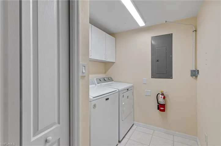 Washroom with cabinets, washer and clothes dryer, light tile patterned flooring, and electric panel