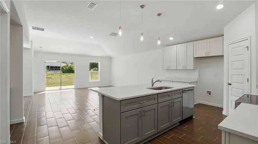 Dual tone kitchen featuring wood finish floors, a kitchen island with sink, lofted ceiling, light stone countertops, and open floor plan
