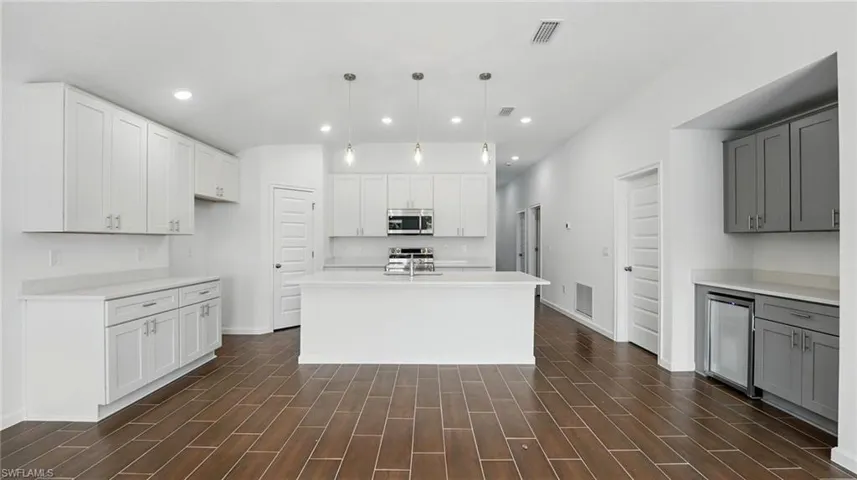 Kitchen with hanging light fixtures, wood tiled floors, a kitchen island with sink, stainless steel appliances, and white cabinetry