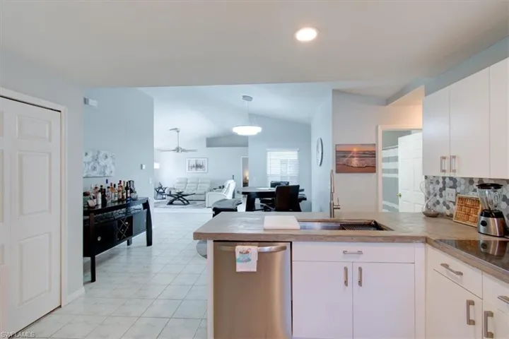 Kitchen featuring stainless steel dishwasher, a peninsula, backsplash, white cabinets, and vaulted ceiling