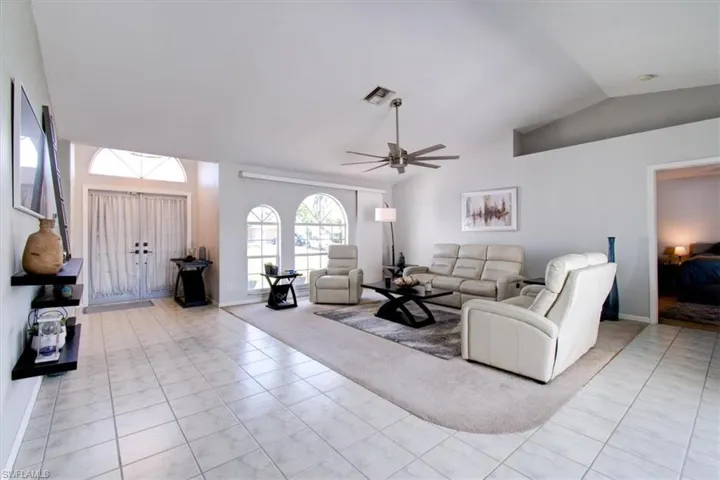 Living room with lofted ceiling, light tile patterned floors, and a ceiling fan