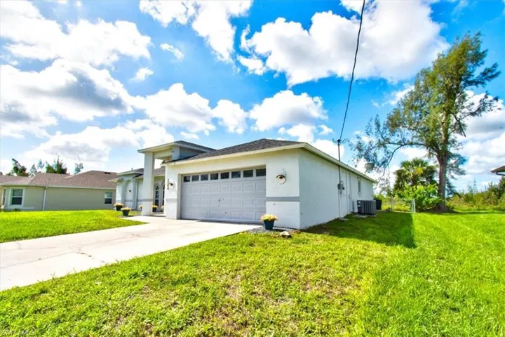View of side of property with an attached garage, concrete driveway, a lawn, and stucco siding