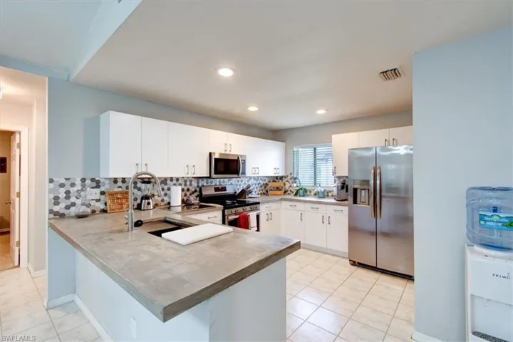 Kitchen featuring appliances with stainless steel finishes, light tile patterned flooring, a peninsula, backsplash, and white cabinetry