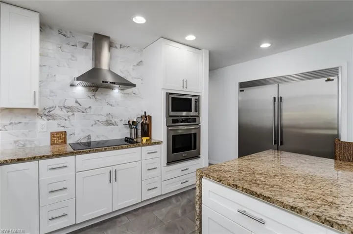Kitchen featuring built in appliances,  stone counters, white cabinets, recessed lighting, and tasteful backsplash