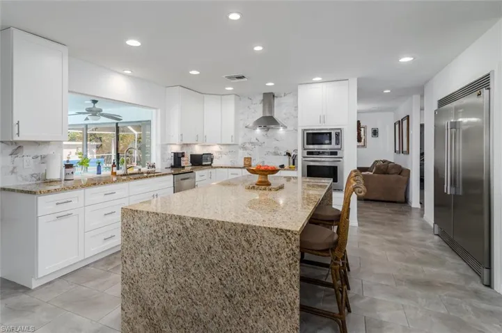 Kitchen featuring light stone counters, white cabinetry, built in appliances, ceiling fan, and a kitchen island