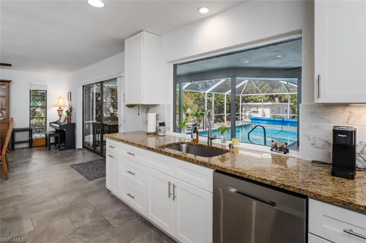 Kitchen with stainless steel dishwasher, white cabinetry, light stone countertops, and recessed lighting