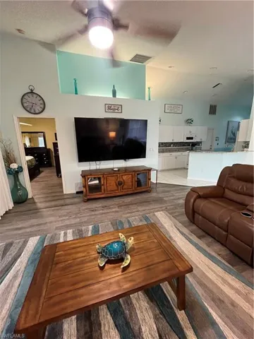 Expansive living area featuring vaulted ceilings, wood-finish flooring, and an open concept layout connecting to the kitchen