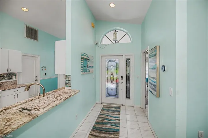 Entryway featuring a decorative glass paneled door with an arched transom, tile flooring, and vaulted ceilings
