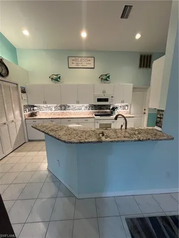 Kitchen featuring a breakfast bar with stone-finish countertops, white cabinetry, a built-in microwave, and tile flooring