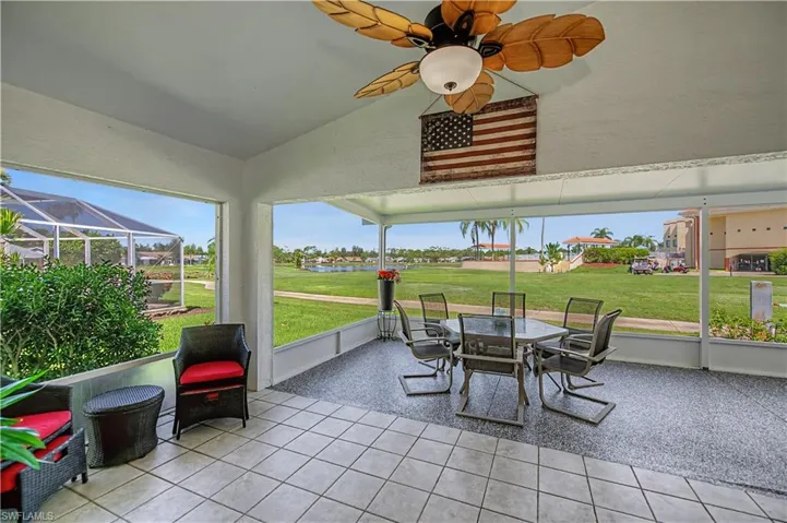 Screened lanai featuring a ceiling fan with leaf-shaped blades, tile flooring, and direct access to an expansive green space with a water feature