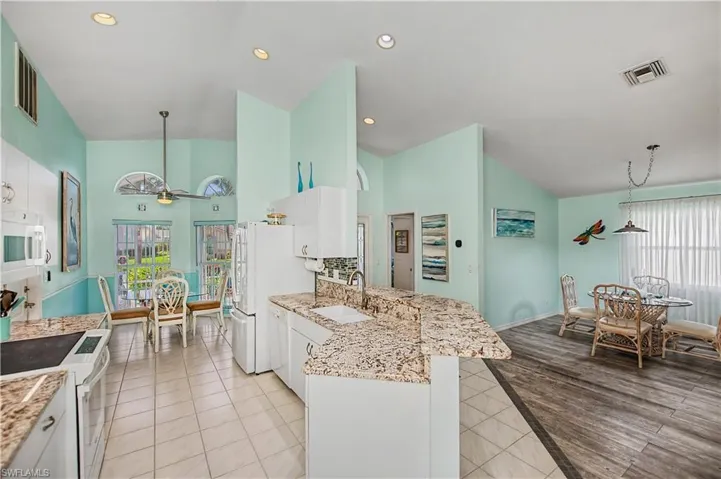 Vaulted ceilings enhance this kitchen featuring white cabinetry, granite countertops, white appliances, and tiled flooring
