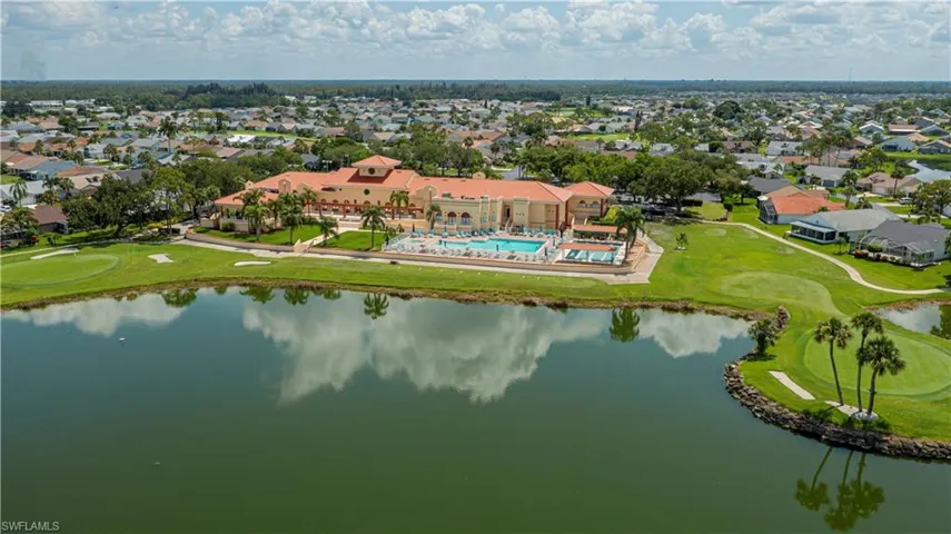 Expansive golf course and lakefront setting featuring a resort-style building with a terracotta tile roof, a large swimming pool, and multiple golf holes with sand traps
