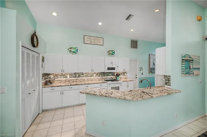Kitchen featuring white cabinetry, granite countertops with a matching backsplash, a breakfast bar, and tile flooring
