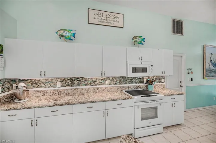 Kitchen featuring extensive white cabinetry, speckled countertops, a tile backsplash, and a built-in microwave
