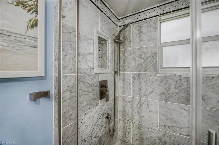 Tiled shower enclosure featuring marbled stone-look wall panels, a built-in niche, and a brushed nickel shower system