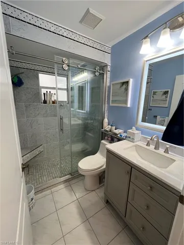 Bathroom featuring a modern vanity with an integrated sink and brushed nickel faucet, a glass-enclosed shower with a built-in bench, and floor-to-ceiling tile work