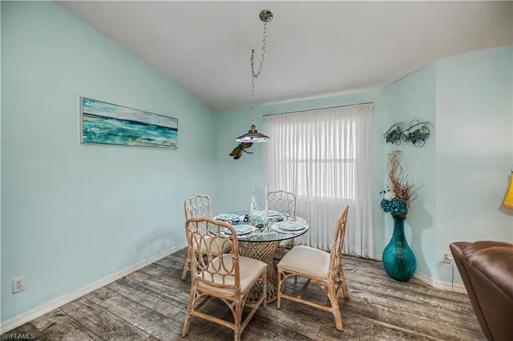 Vaulted ceiling dining area featuring wood-finish flooring, a window with sheer window treatments, and a ceiling-mounted light fixture
