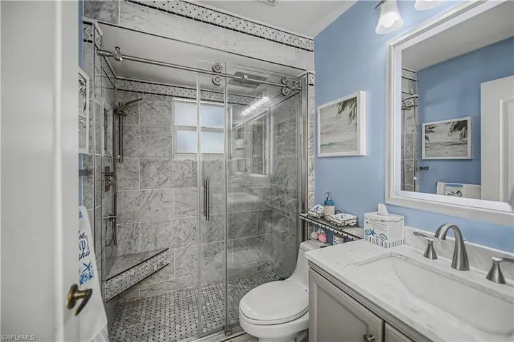 Spacious shower enclosure with glass sliding doors, marble-finish wall tiling, and a built-in shower bench