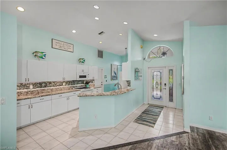 Kitchen with white cabinetry, integrated microwave, and multi-toned backsplash
