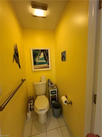 Compact powder room featuring a toilet, white tile flooring, and a wall-mounted grab bar