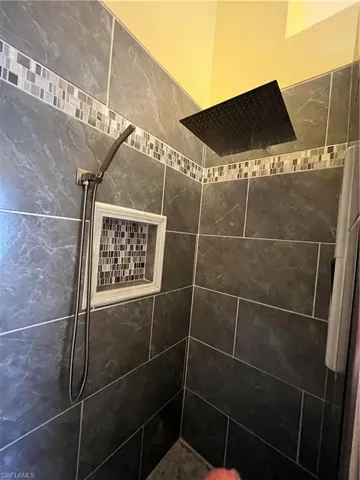 Contemporary shower enclosure featuring dark large-format wall tiles with mosaic accent banding, a built-in shower niche with mosaic backing, and a dark finish rain shower head