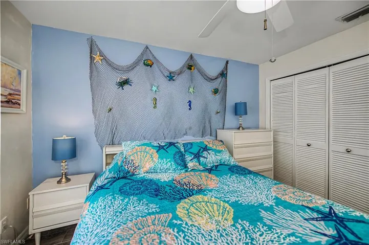 Bedroom featuring a light blue accent wall, white louvered bifold closet doors, a ceiling fan, and wood-finish flooring