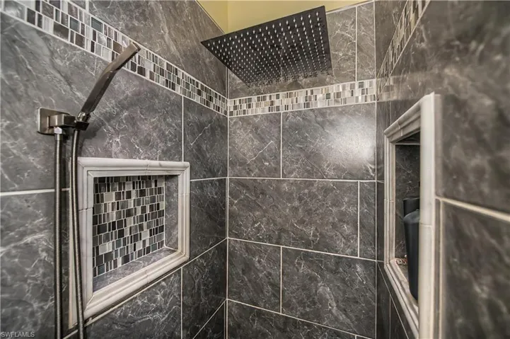 Tiled shower enclosure featuring a rectangular rain showerhead and a handheld shower fixture