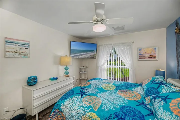 Recessed window with vertical blinds, wood-finish flooring, ceiling fan with integrated lighting, wall-mounted television, and a built-in corner shelf