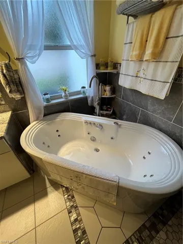 Freestanding jetted bathtub with an integrated faucet, surrounded by large format tile walls and hexagonal floor tiles with a mosaic accent