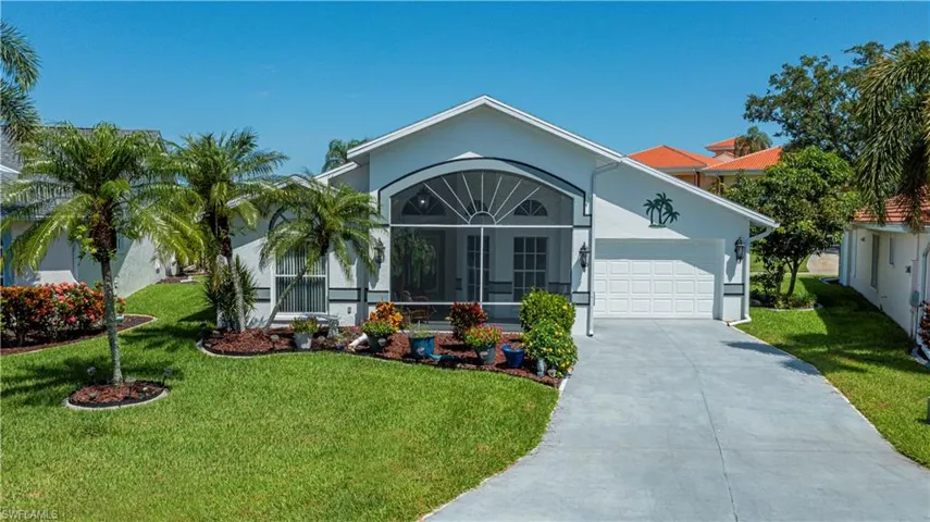 Single-story white stucco residence with a screened entry, an attached two-car garage, a concrete driveway, and a manicured lawn with mature palm trees and landscaping