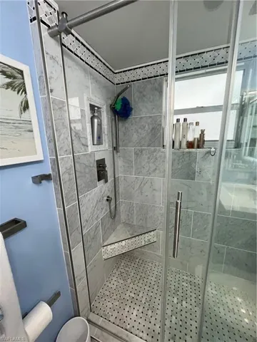 Tiled shower enclosure featuring a corner bench, integrated shower niche, and glass door