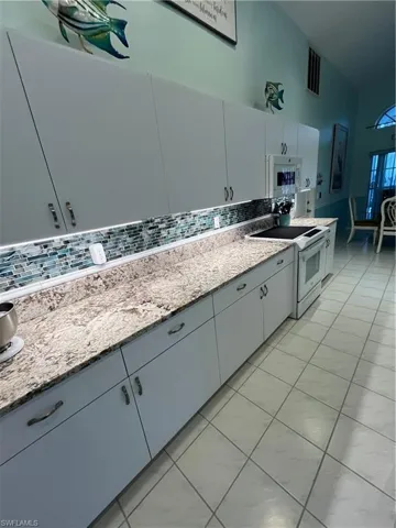 Kitchen featuring extensive light cabinetry, stone-finish countertops, a glass tile backsplash, under-cabinet lighting, and tile flooring
