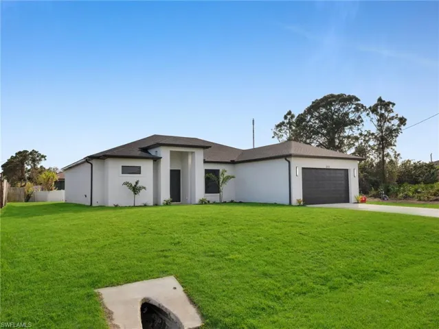 Prairie-style house with driveway, a garage, fence, a front lawn, and stucco siding