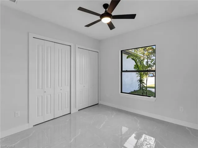 Unfurnished bedroom with multiple closets, marble finish floor, baseboards, and a ceiling fan