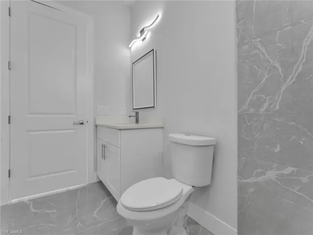 Full bathroom with toilet, marble finish floor, baseboards, and vanity
