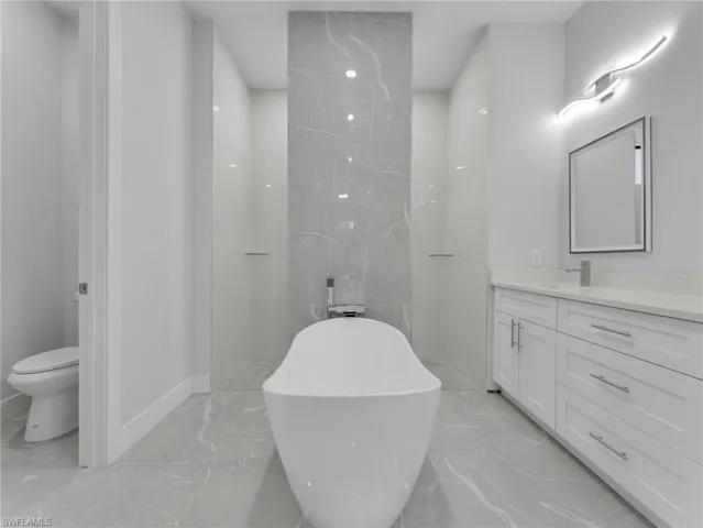 Bathroom featuring toilet, marble finish floor, a freestanding bath, and vanity