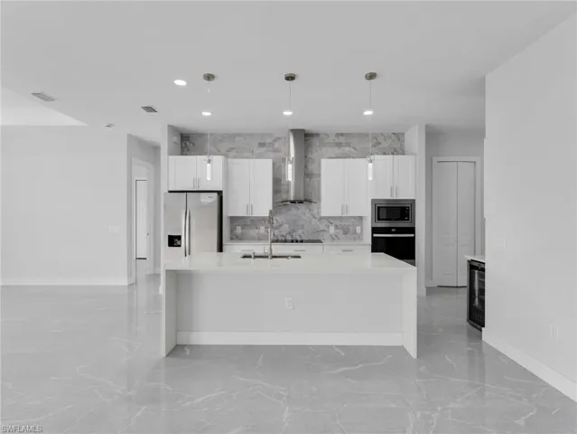 Kitchen with wall chimney exhaust hood, appliances with stainless steel finishes, decorative light fixtures, light countertops, and white cabinetry