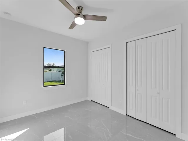 Unfurnished bedroom featuring multiple closets, marble finish floor, baseboards, and a ceiling fan