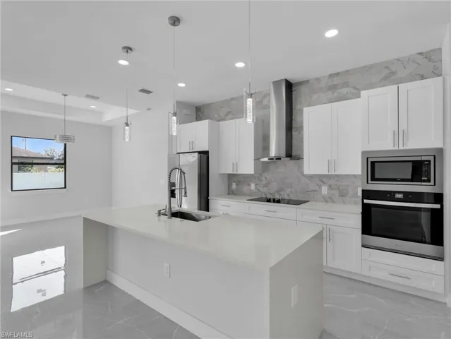 Kitchen with hanging light fixtures, wall chimney range hood, white cabinetry, and stainless steel appliances