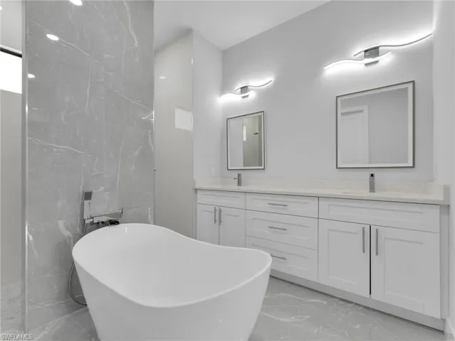 Full bathroom with double vanity, marble finish floor, a sink, and a soaking tub
