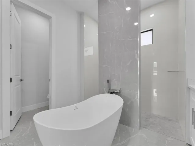 Full bath featuring marble finish floor, vanity, and a soaking tub