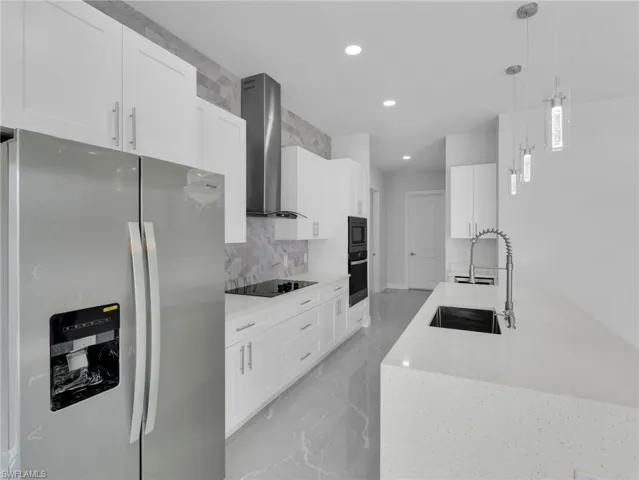 Kitchen featuring appliances with stainless steel finishes, pendant lighting, white cabinetry, and wall chimney exhaust hood