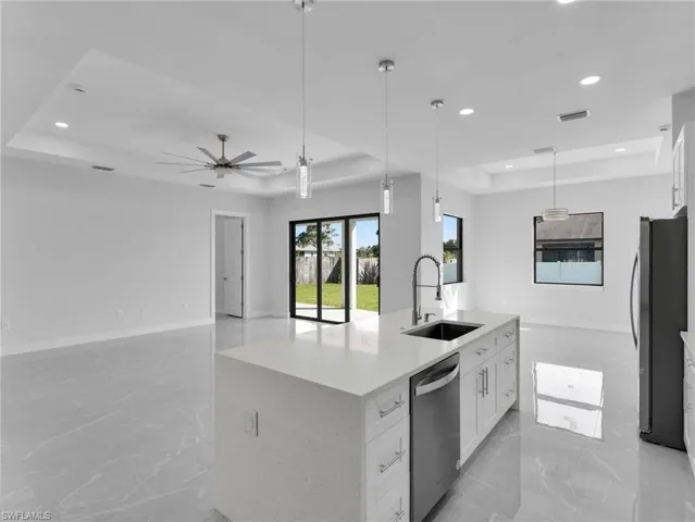 Kitchen with stainless steel appliances, a tray ceiling, white cabinets, and a center island with sink