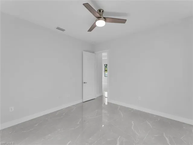 Empty room with marble finish floor, baseboards, visible vents, and a ceiling fan
