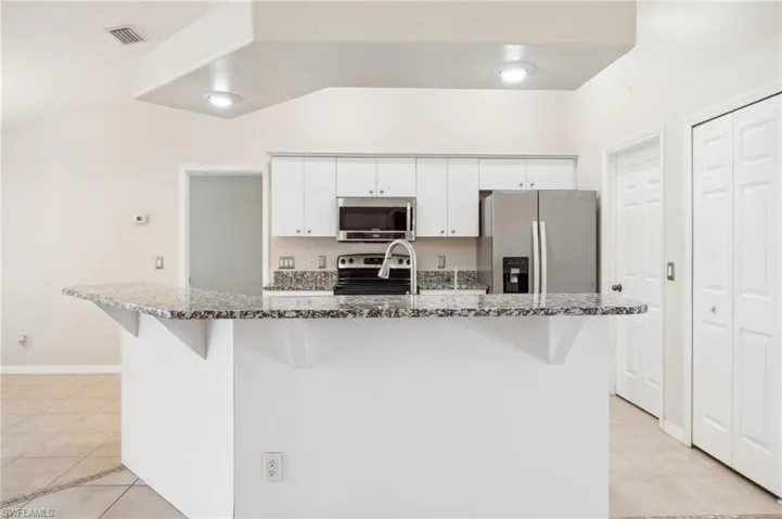 Kitchen with white cabinets, stone counters, stainless steel appliances, lofted ceiling, and a center island with sink