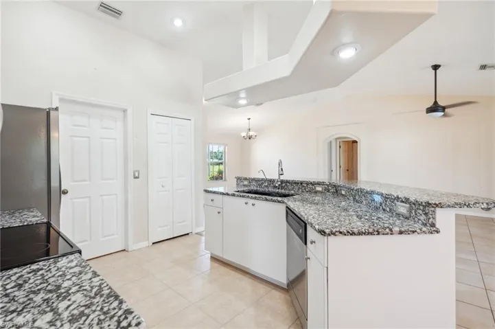 Kitchen featuring ceiling fan with notable chandelier, appliances with stainless steel finishes, stone countertops, white cabinetry, and sink
