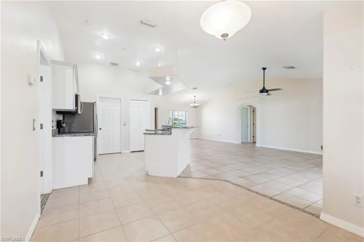 Kitchen featuring stone counters, ceiling fan, vaulted ceiling, and white cabinetry
